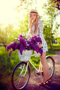 Hasır şapkalı mutlu güzel bir kadının portresi klasik bir bisiklet ve açık havada park arka planında çiçekler..