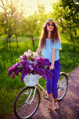 Hasır şapkalı mutlu güzel bir kadının portresi klasik bir bisiklet ve açık havada park arka planında çiçekler..