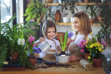 Sevimli bir kız çocuğu annesinin bitkilere bakmasına yardım eder..