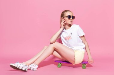 Pembe arka planda kaykayı olan neşeli bir genç kız.