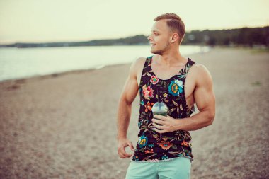 Sahilde parlak giysiler içinde genç yakışıklı bir adam, ferahlatıcı bir kokteyl içiyor ve tatilinin tadını çıkarıyor..