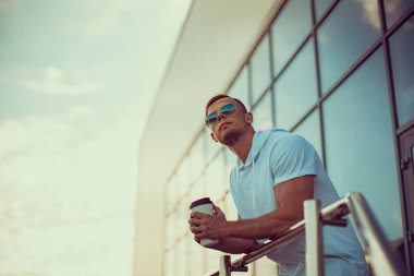 Şehir merkezinin yanındaki genç yakışıklı bir adam elinde bir fincan kahveyle yukarı bakıp bir şeyler hayal ediyor.