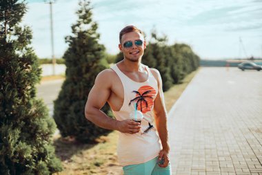 Parlak elbiseli, genç ve yakışıklı bir adam sokakta yürüyor. Serinletici bir kokteyl içiyor ve tatilinin tadını çıkarıyor..