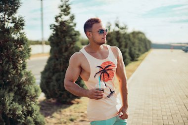 Parlak elbiseli, genç ve yakışıklı bir adam sokakta yürüyor. Serinletici bir kokteyl içiyor ve tatilinin tadını çıkarıyor..