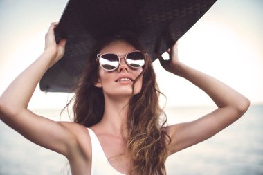 Beyaz mayo ve pembe şapkalı modern esmer kumsalda ayakta duruyor.