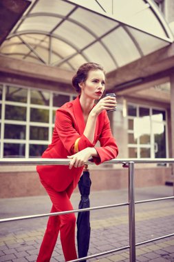 Ofis yakınında cep telefonu kullanan kırmızı kostümlü bir iş kadını, cep telefonu takan bir kız, modern banka binasının yakınında akıllı telefondan mesaj atan bir bayan yönetici.