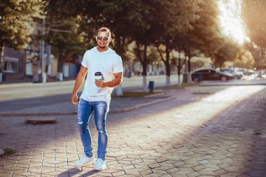 Adam şehirde dolaşıyor ve kahve içiyor. Yakışıklı bir adam yürüyor ve dinleniyor.