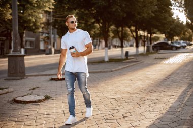 Adam şehirde dolaşıyor ve kahve içiyor. Yakışıklı bir adam yürüyor ve dinleniyor.