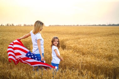 Güzel bir buğday tarlasında Amerikan Bayrağı taşıyan anne ve kızı
