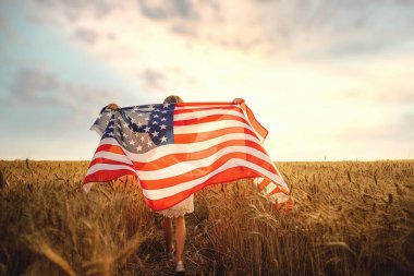 Beyaz elbiseli bir kızın, güzel bir buğday tarlasında koşarken Amerikan bayrağı taktığı arka plan görüntüsü.