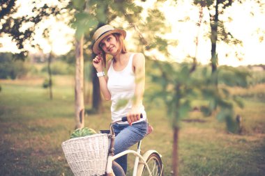 Hasır şapkalı, parkta bisikletli güzel bir kız.