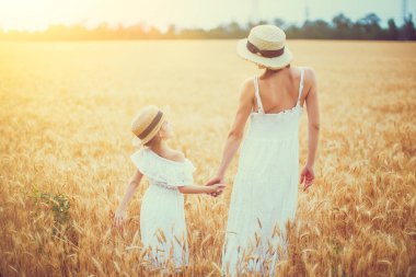 Genç anne ve kızı beyaz elbiseli ve hasır şapkalı.