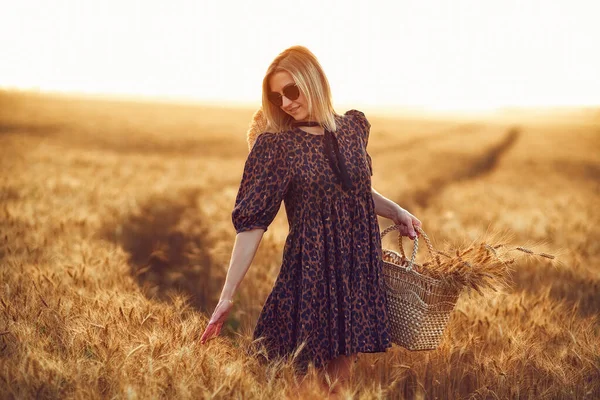 woman in animal print dress, straw hat in front of Sun in middle