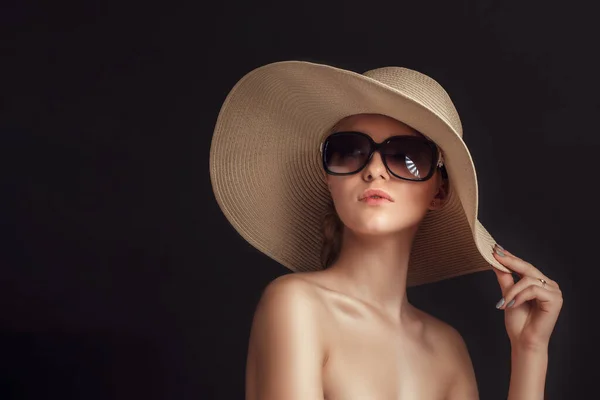 Bellezza foto di donna attraente indossando cappello di paglia e grandi occhiali da sole in posa su sfondo scuro studio — Foto Stock