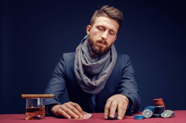 Siyah kumarhanede oynayan, puro içen, viski içen şık sakallı adam.