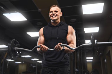 Yakışıklı ve kaslı bir adam, spor salonunda kameraya poz veriyor.