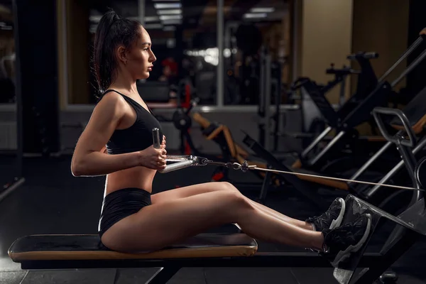 Musculaire fitness vrouw atleet doet zware gewicht oefening voor terug op de machine met kabel in de sportschool — Stockfoto
