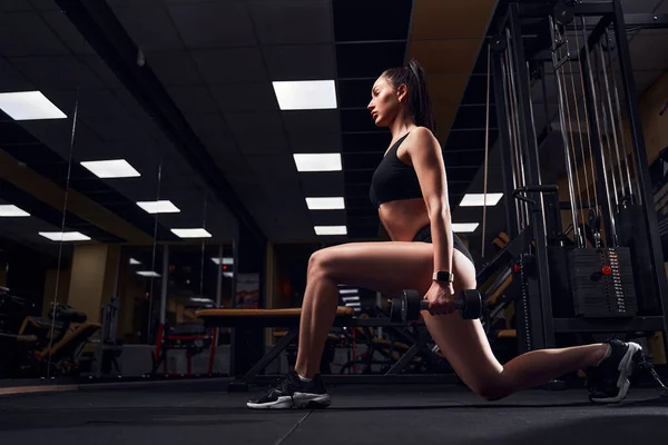 Slim fit vrouw doet lunges met halters in haar handen in een moderne sportschool — Stockfoto