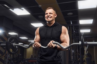 Yakışıklı ve kaslı bir adam, spor salonunda kameraya poz veriyor.