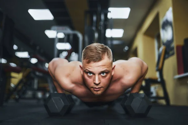 Un joven atlético haciendo flexiones en el gimnasio. Musculoso y fuerte chico haciendo ejercicio —  Fotos de Stock