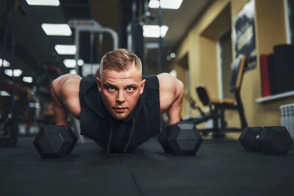 Un joven atlético haciendo flexiones en el gimnasio. Musculoso y fuerte chico haciendo ejercicio —  Fotos de Stock