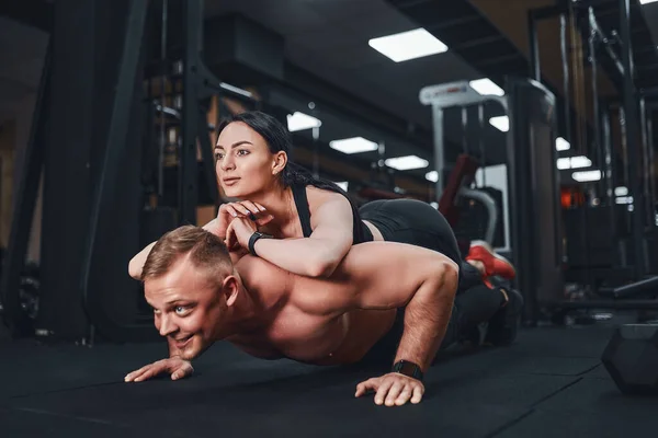 Jovem homem musculoso fazendo exercício push-up e segurando menina. formação conjunta. Aulas de grupo. Edifício de equipa. romance. — Fotografia de Stock