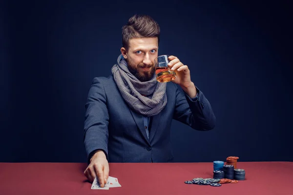 Stilvoller bärtiger Mann in Anzug und Schal spielt im dunklen Casino, raucht Zigarre, trinkt Whiskey — Stockfoto