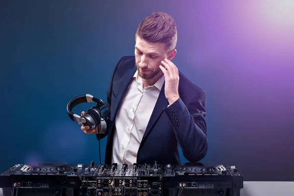 Hombre DJ en traje oscuro reproducir música en un mezclador de Djs. Grabado en estudio. Fondo azul oscuro —  Fotos de Stock