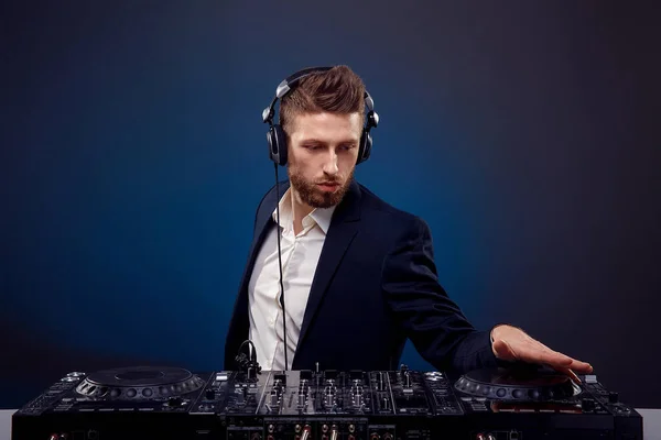 Hombre DJ en traje oscuro reproducir música en un mezclador de Djs. Grabado en estudio. Fondo azul oscuro —  Fotos de Stock