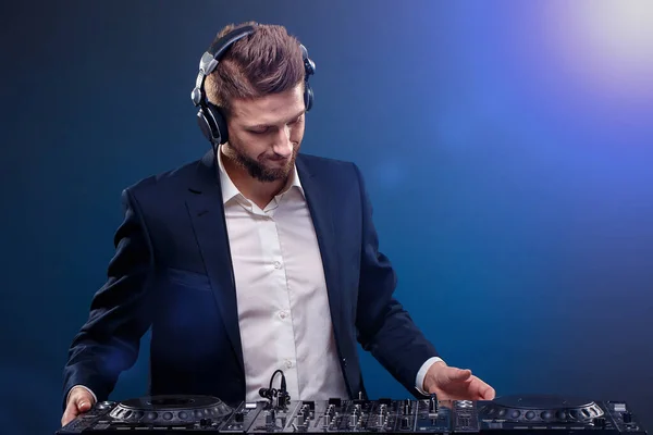 Ein DJ im dunklen Anzug legt Musik auf einem DJ-Mischpult auf. Studioaufnahmen. Dunkelblauer Hintergrund — Stockfoto