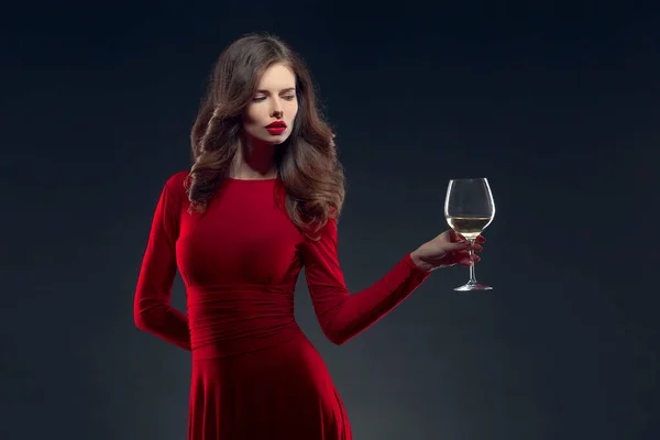밝은 메이크업을 하고 머리 스타일에 빨간 드레스를 입고 어두운 배경에 포도나무 잔을 들고 포즈를 취하고 고립된 여성 — 스톡 사진