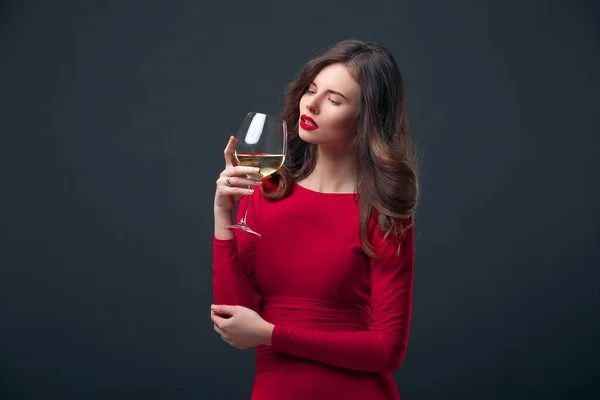 Woman with bright makeup, hairstyle wearing red dress posing with glass of vine over dark background, isolate — Stock Photo, Image