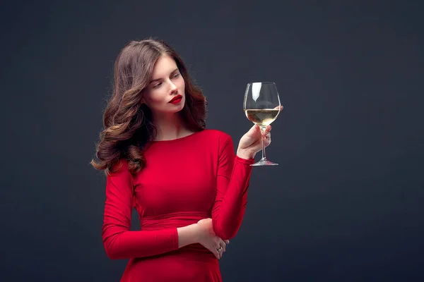Woman with bright makeup, hairstyle wearing red dress posing with glass of vine over dark background, isolate — Stock Photo, Image