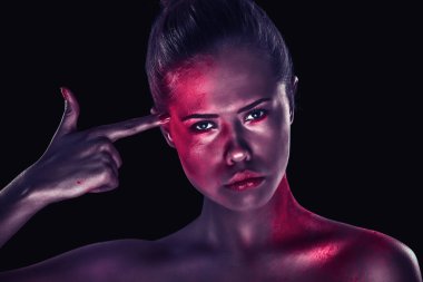 Esmer arka planda sanatsal makyajlı bir kadın parmağıyla şakağına dokunuyor.