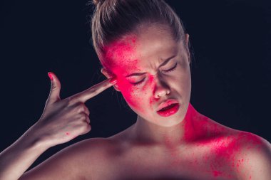 Esmer arka planda sanatsal makyajlı bir kadın parmağıyla şakağına dokunuyor.