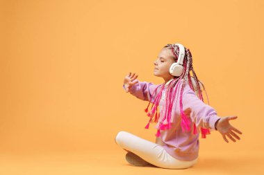 Yuvarlak gözlüklü, pembe rasta giyen sevimli çocuğun arka görüntüsü.