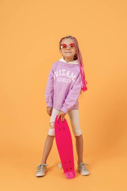 Aktif genç kız pembe gömlekli ve beyaz şortlu elinde kaykayla