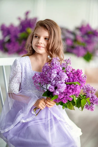 Hermosa niña de edad preescolar en un vestido delicado sentado en un columpio decorado con flores de color lila. — Foto de Stock