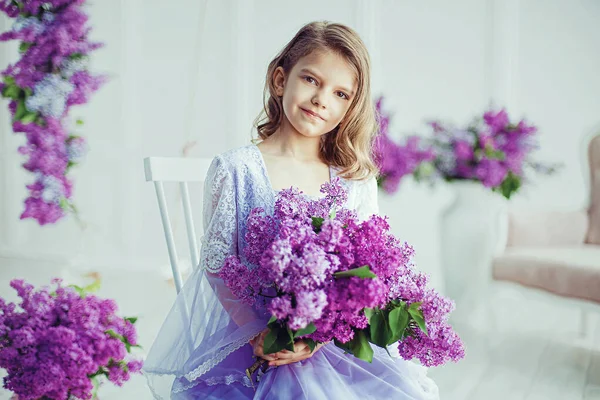 Menina bonita da idade pré-escolar em um vestido delicado sentado em um balanço decorado com flores de lilás. — Fotografia de Stock