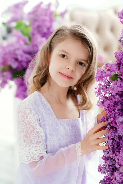 Belle petite fille d'âge préscolaire dans une robe délicate assise sur une balançoire décorée de fleurs de lilas. — Photo