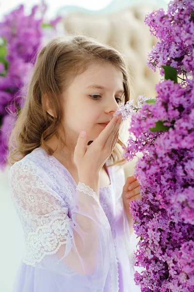 Belle petite fille d'âge préscolaire dans une robe délicate assise sur une balançoire décorée de fleurs de lilas. — Photo