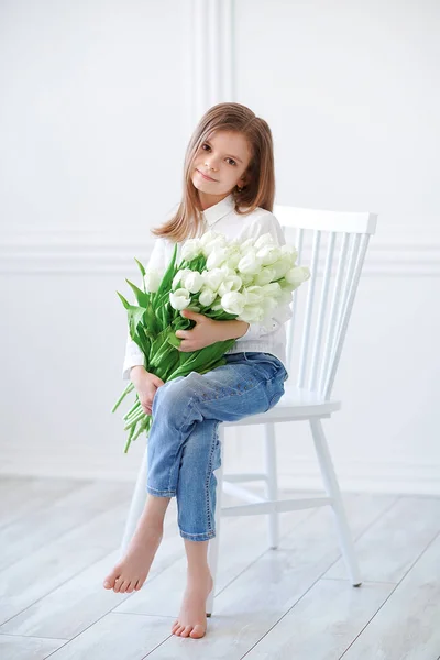Портрет красивой красивой девушки с белыми цветами тюльпаны сидят на стуле, улыбаясь. Фото в помещении — стоковое фото