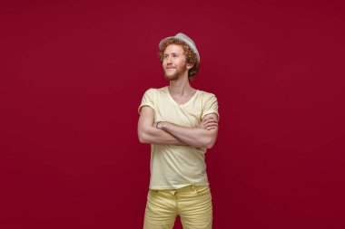 Modayı takip eden hippi stüdyoda kollarını kavuşturmuş poz veriyor. Hasır şapkalı gülen adam kırmızı arka planda izole edilmiş kameradan yüzünü çeviriyor.