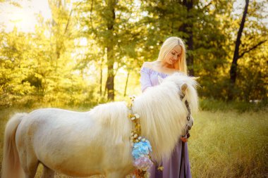 Mor elbiseli kadın beyaz tek boynuzlu ata sarılıyor. Hayaller gerçek olur.