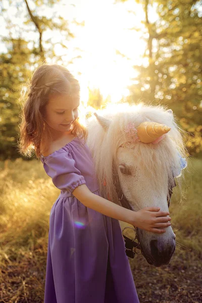 穿着紫色衣服的女孩抱着白色独角兽马。梦想来了 — 图库照片