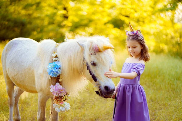 Meisje in paarse jurk met krans van een eenhoorn in haar knuffelen wh — Stockfoto