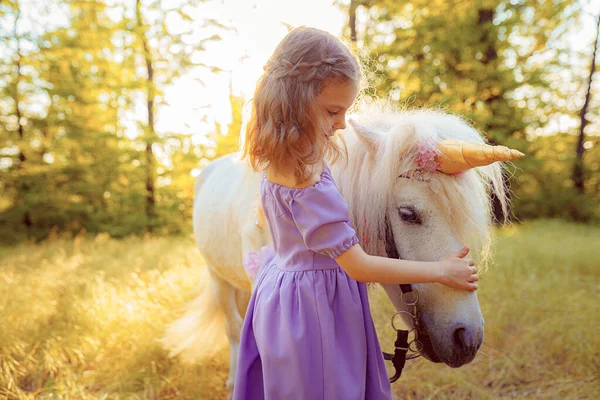 穿着紫色衣服的女孩抱着白色独角兽马。梦想来了 — 图库照片