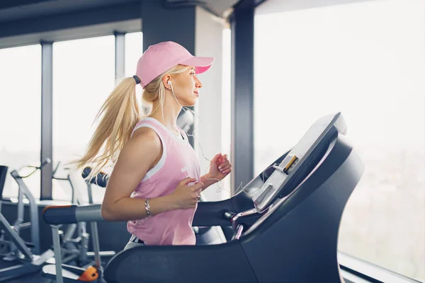 Vista lateral de la mujer rubia deportiva haciendo ejercicio en la cinta de correr en el gimnasio —  Fotos de Stock