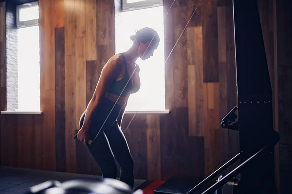 Determined young woman working out on row machine in fitness stu