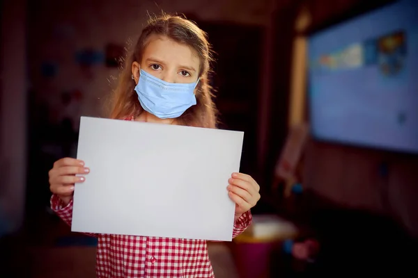 Liten flicka i en skyddande mask, pyjamas håller ett tomt ark av — Stockfoto